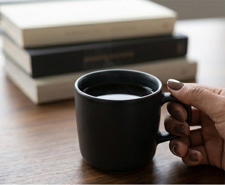 A black mug of coffee beside a stack of books